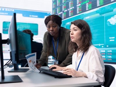 Diverse team of analysts examining monthly cost and revenue elements on a big screen, working on creating a financial projection for future improvements and success within the organization.